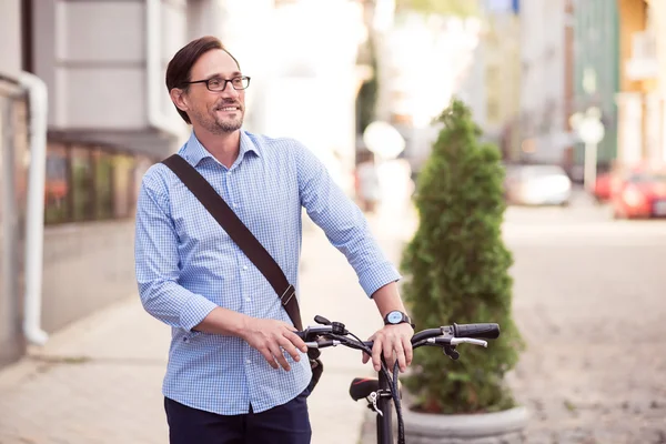 Agradable hombre sonriente sosteniendo la bicicleta — Foto de Stock