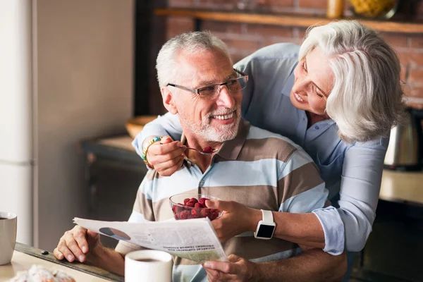 Счастливые бабушка и дедушка разговаривают и смеются во время еды на кухне — стоковое фото