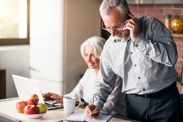 Happy family in their sixties using technologies at the kitchen — Stock Photo, Image