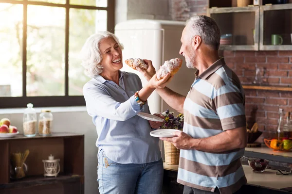 Пожилая пара, развлекающаяся на кухне во время завтрака — стоковое фото