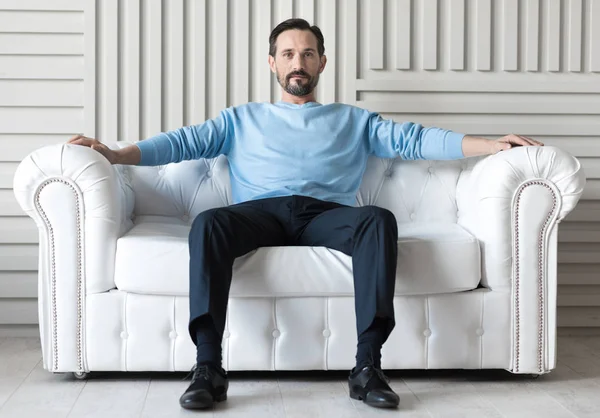 Selbstbewusster schöner Mann sitzt auf einem Sofa — Stockfoto