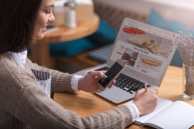 Memnun kadın yapım notları gülümseyen ve cep telefonu kullanarak.