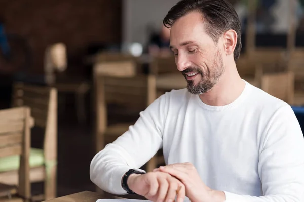 Sonriente hombre barbudo comprobando el tiempo en la cafetería — Foto de Stock