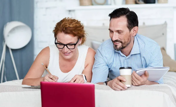 Paar benutzt Laptop auf dem Bett und macht sich Notizen — Stockfoto