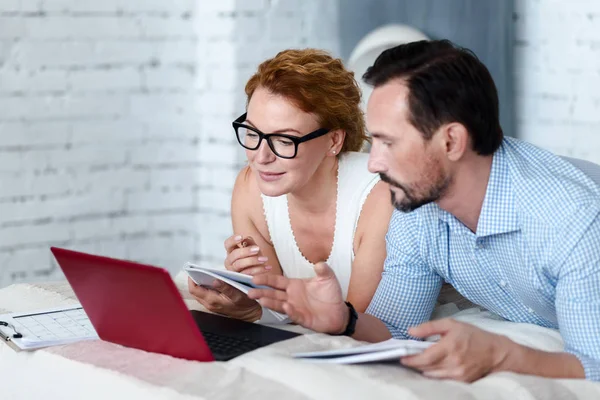 Couple using laptop on bed and making notes