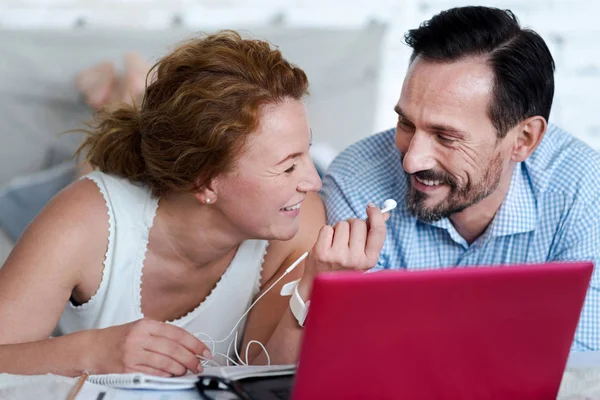 Vrouw oortelefoons te geven aan de mens terwijl liggend op bed — Stockfoto