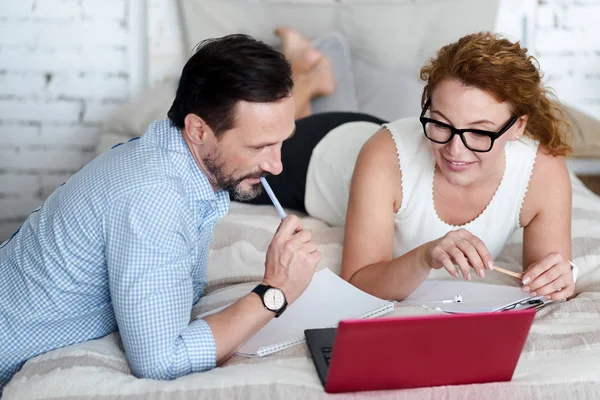 Pareja usando el ordenador portátil en la cama y tomando notas — Foto de Stock