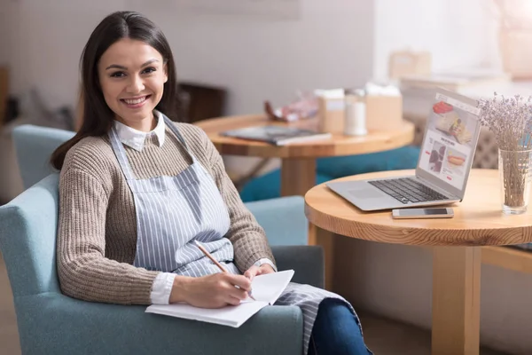 Mujer bastante sonriente sentada en el sillón y tomando notas . — Foto de Stock