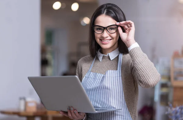 Jovem mulher positiva sorrindo e segurando laptop . — Fotografia de Stock