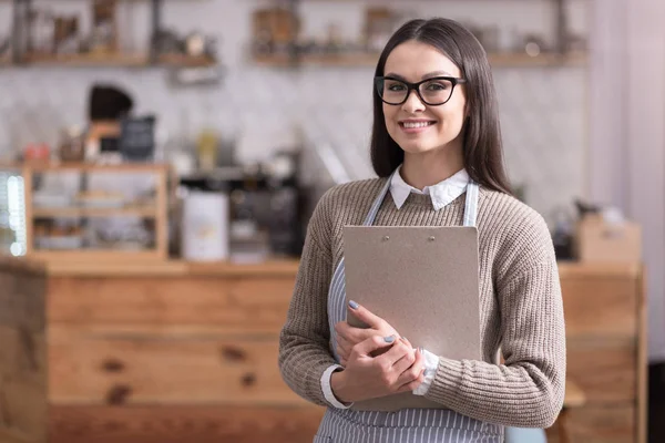 Bastante mujer con gafas sonriendo y sosteniendo la carpeta . —  Fotos de Stock