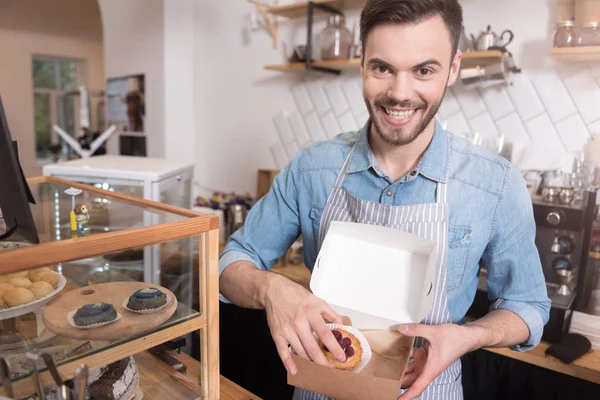 Positive handsome waiter putting cakes into the box. — Stock Photo, Image
