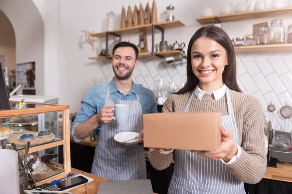 Charming smiling waiters holding cup and box. — Stock Photo, Image