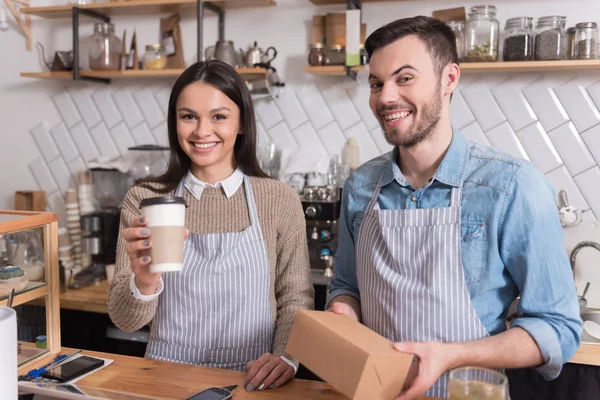 Felices camareros sonrientes sosteniendo taza y caja . — Foto de Stock