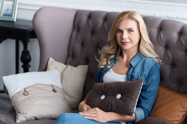 Hübsche blonde Frau sitzt auf grauem Sofa — Stockfoto