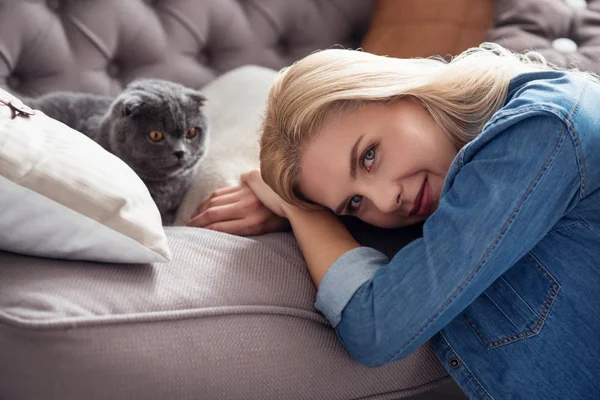 Süße blonde Dame mit ihrer Katze auf der Couch — Stockfoto