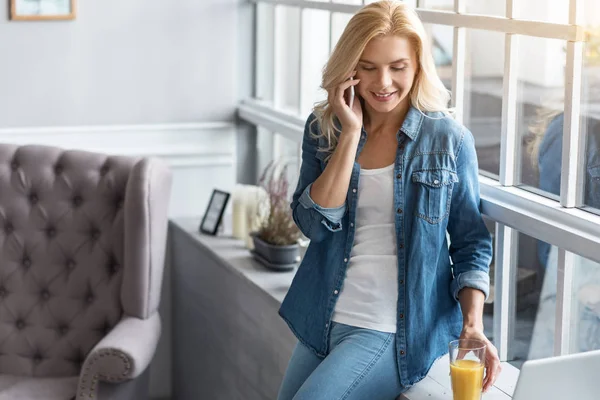 Szőke nő beszél egy ablak közelében mobiltelefon — Stock Fotó