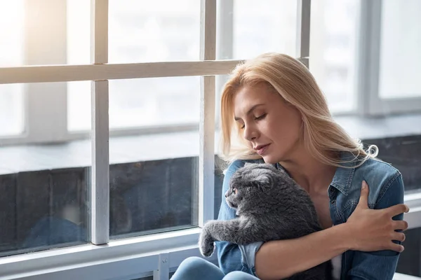 Блондинка держит кота у окна . — стоковое фото