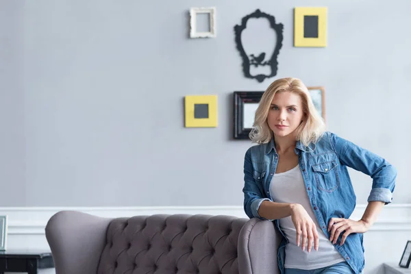 Blonde Frau lehnt auf grauem Sofa — Stockfoto