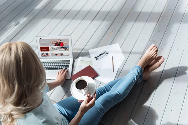 Vista superior de la mujer sosteniendo la taza de café y utilizando el ordenador portátil —  Fotos de Stock