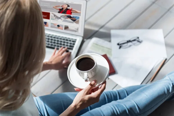 Kobieta trzyma kubek kawy i za pomocą laptopa z bliska — Zdjęcie stockowe
