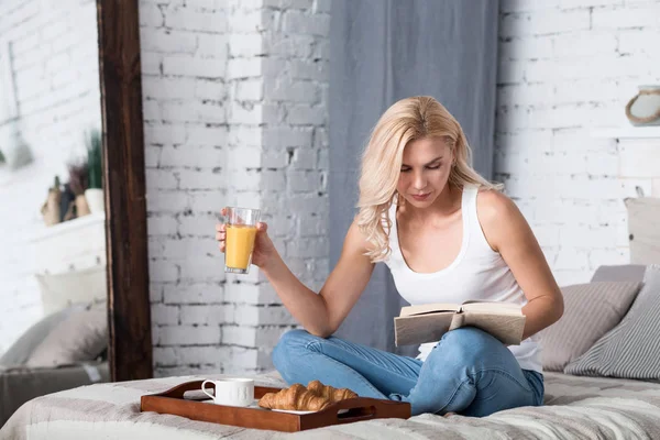 Blond lady having breakfast and reading book — Stock Photo, Image