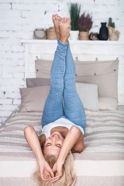 Blonde vrouw met benen omhoog op bed — Stockfoto