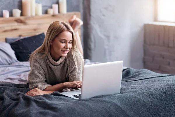 Mulher bonita deitada na cama com um laptop — Fotografia de Stock