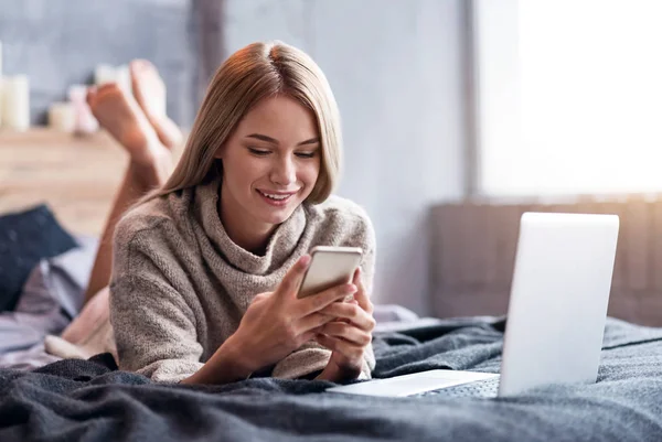 Donna deliziata utilizzando smartphone e laptop a letto — Foto Stock