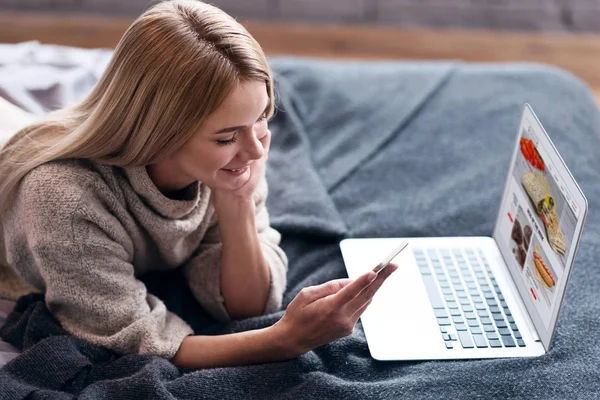 Genç kadın yatakta bir smartphone yazarak — Stok fotoğraf