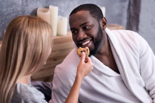 Mulher loira alimentando seu namorado africano com biscoitos — Fotografia de Stock