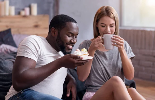 Overjoyed couple drinking tea with cupcakes in bedroom — Stock Photo, Image