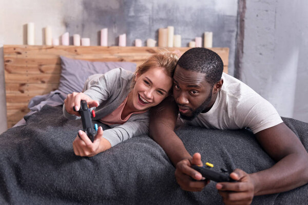 Радостная пара, играющая в видеоигры в постели
