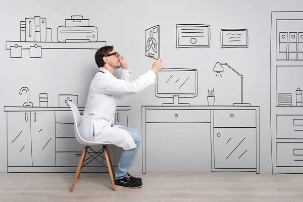 Médico concentrado sentado en la silla y mirando la foto . —  Fotos de Stock