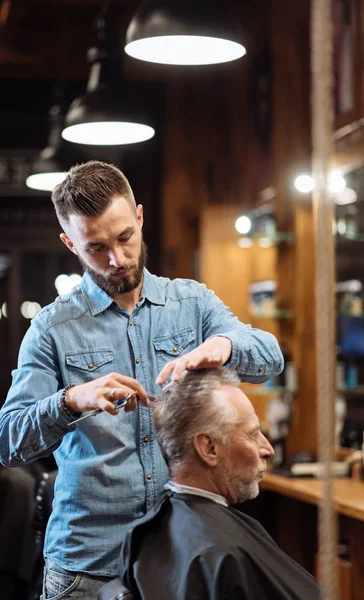 Viejo hombre teniendo corte de pelo por joven especialista — Foto de Stock