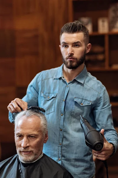 Pohledný vousatý kadeřník sušení vlasů klienta — Stock fotografie