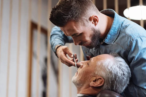 Knappe jonge Kapper snijden snor voor senior client met een schaar — Stockfoto