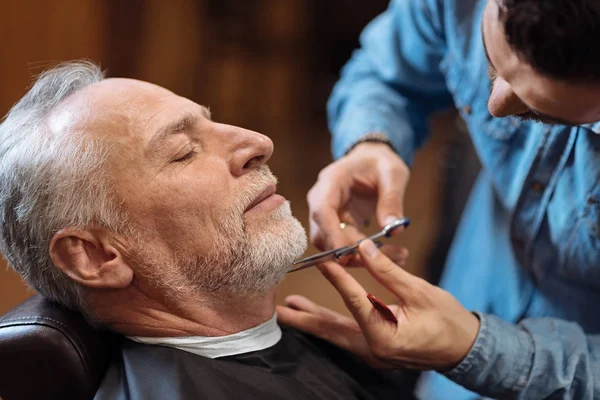 Парикмахерская стрижка бороды старшего клиента ножницами — стоковое фото
