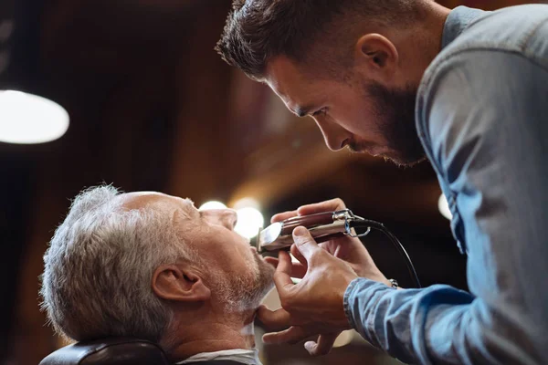 Side view of young barber trimming beard — Stock Photo, Image