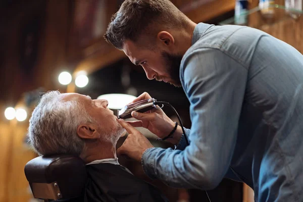 Side view of young barber trimming beard — Stock Photo, Image