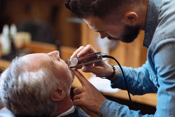 Side view of young barber trimming beard — Stock Photo, Image