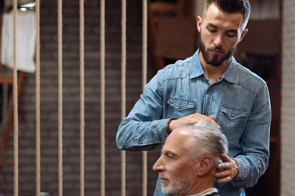 Красивый парикмахер делает массаж головы старшему клиенту — стоковое фото