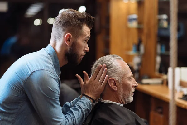 Handsome barber styling hair of senior man — Stock Photo, Image