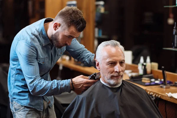Красивый парикмахер стрижет волосы старика — стоковое фото