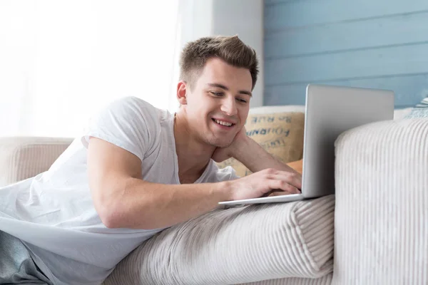 Sonriendo joven hombre positivo utilizando el ordenador portátil . —  Fotos de Stock