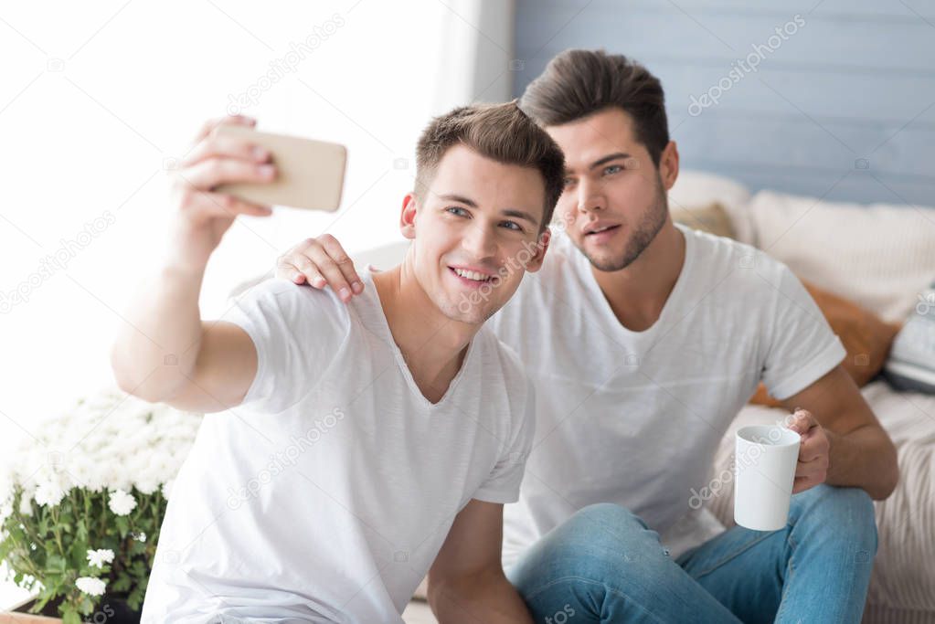 Young smiling gay couple taking selfie.