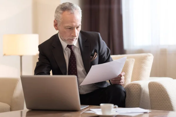 Вовлеченный бизнесмен, работающий с бумагами и сидящий в отеле — стоковое фото