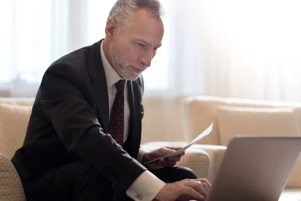 Lächelnder Geschäftsmann, der mit Papieren arbeitet und auf den Laptop schaut — Stockfoto