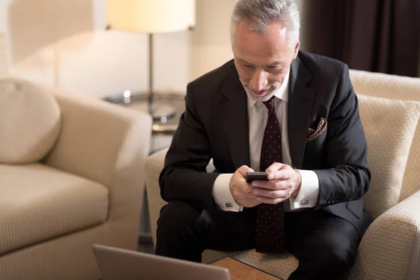 Радостный бизнесмен держит мобильный телефон перед ноутбуком — стоковое фото