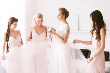 Amused bridesmaids touching the dress of the bride clipart