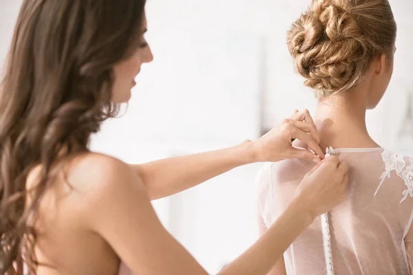 Charming bridesmaid helping the bride with her dress — Stock Photo, Image